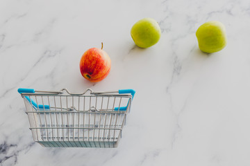 grocery store mini shopping basket with one single red apple among other green ones