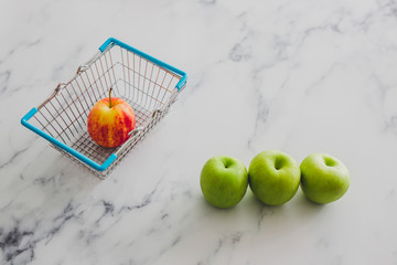 grocery store mini shopping basket with one single red apple among other green ones
