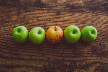 one single red apple among other green ones on wooden table