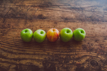 one single red apple among other green ones on wooden table