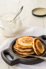 Homemade fried fritters on a small round wooden plate, next to a jar of sour cream on an old table. 