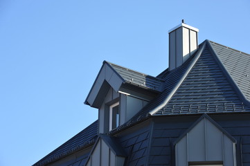 Frisch renoviertes, mit grauen Metallschindeln gedecktes Haus mit Aufkeilfenstern/Gaubenfenstern und Schornstein mit Stehfalz-Metallverkleidung und Schneefang, regenfallrohr und Dachrinne