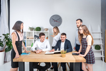 Theme is business and teamwork. A group of young Caucasian people office workers holding a meeting, briefing, working with papers and documents in a light office office around a wooden table