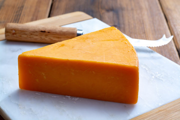 Piece of bright yellow hard cheese cheddar, originating in the English village of Cheddar in Somerset