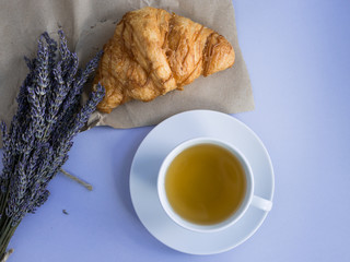 Cup with lavender tea and fresh croissant on gray background