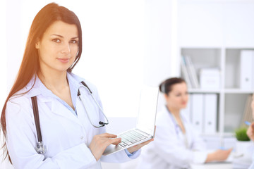 Brunette female doctor on the background of colleagues talking to each other in hospital. Medicine and health care concept