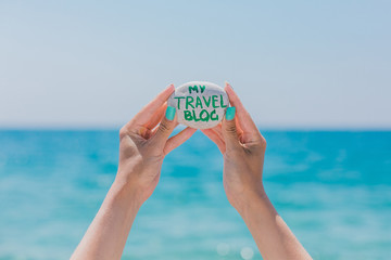 Girl holding pebble stone with sign about travel theme. My travel blog. Traveling blog. Sea holidays. Sea pebbles on the sea background