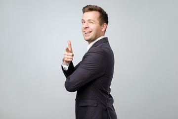 Young caucasian man in suit pointing at camera like saying You are right dude