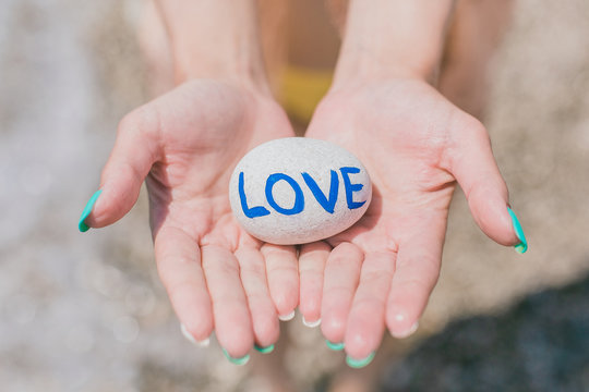 Girl holding in palms round stone pebble with sign love.
