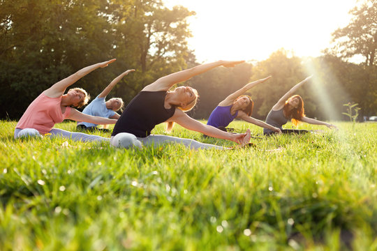 Mixed Age Group Of People Practicing Yoga Outside In The Park While Sunset
