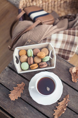 A cup of hot tea, macaroons, a knitted sweater, a hat, a rug on a wooden table. Autumn. Winter. Cozy.