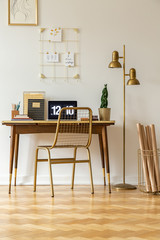 Gold chair at desk with laptop in white home office interior with lamp and poster. Real photo