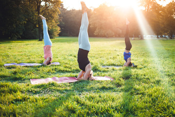 Yoga at park, group of mixed age women doing salamba sirsasana pose headstand exercise
