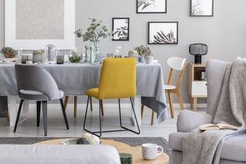 Yellow chair next to a table in a grey dining room interior. Real photo
