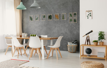 Open space living and dining room interior with wooden furniture, stylish decor and a plant leaves gallery on a gray wall