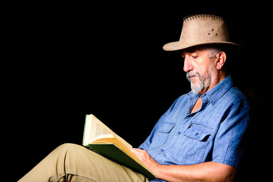 Adult man with hat reading an old book on black background