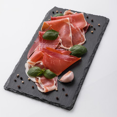 Italian prosciutto crudo or spanish jamon on a stone plate white background