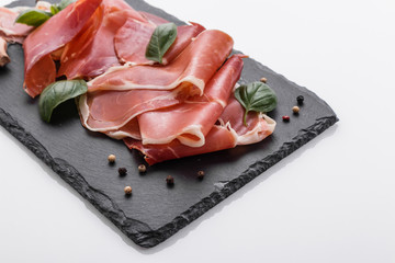 Italian prosciutto crudo or spanish jamon on a stone plate white background