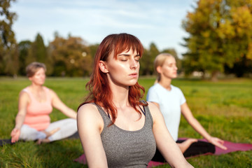 Yoga in the park, young woman doing exercises with group of mixed age people
