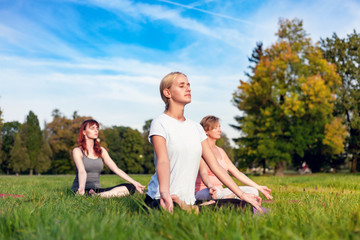 Fototapeta premium Yoga in the park, young woman doing exercises with group of mixed age people