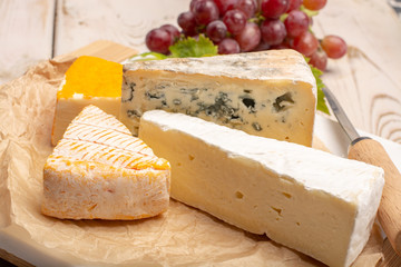Tasting plate with four France cheeses, cream brie, marcaire, saint paulin and blue auvergne cheese, served with fresh ripe grapes