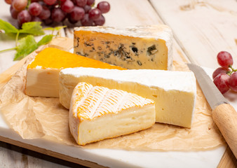 Tasting plate with four France cheeses, cream brie, marcaire, saint paulin and blue auvergne cheese, served with fresh ripe grapes