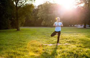 Yoga in the park, young woman doing tree pose vrksasana
