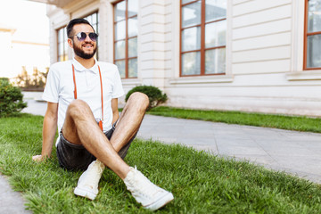 Fototapeta premium Stylish hipster with a camera on his neck, sitting on the lawn in the Park