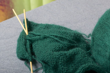 Knitting with wooden knitting. A ball of dark green thread and wooden knitting needles in an unfinished knit.