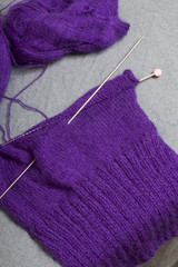 Knitting with steel knitting needles. A ball of purple thread and steel knitting needles in an unfinished knit.