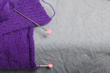 Knitting with steel knitting needles. A ball of purple thread and steel knitting needles in an unfinished knit.