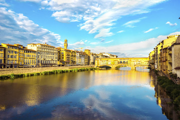 Panoramic view of the Arno River and stone medieval bridge Ponte Vecchio with beautiful reflection of colorful houses and blue sky with porous clouds, Florence, Tuscany, Italy.