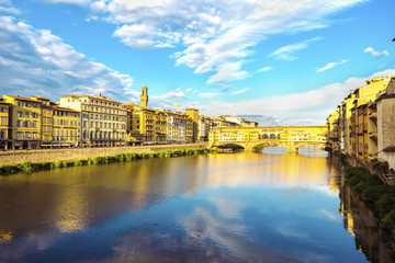 Naklejka premium Panoramic view of the Arno River and stone medieval bridge Ponte Vecchio with beautiful reflection of colorful houses and blue sky with porous clouds, Florence, Tuscany, Italy.