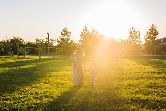 Beautiful woman with daughter and baby son on green grass field. Mother with two little children walking outdoors. Happy family concept