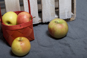 Ripe aromatic apples on a gray cloth. Nearby is a wooden box, knocked out of the boards.