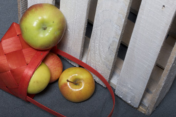 Ripe aromatic apples from a wicker basket on a gray cloth. Nearby is a wooden box, knocked out of the boards.