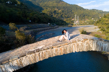 A girl is sitting on an ancient stone bridge.