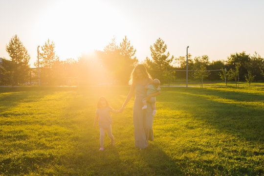 Beautiful woman with daughter and baby son on green grass field. Mother with two little children walking outdoors. Happy family concept