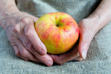 A ripe apple in the hands of an old woman.