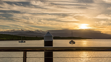 Naklejka na ściany i meble Cloudy sunset over ocean and boats with timber pylon