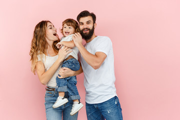 A happy family on pink studio background. The father, mother and son posing together