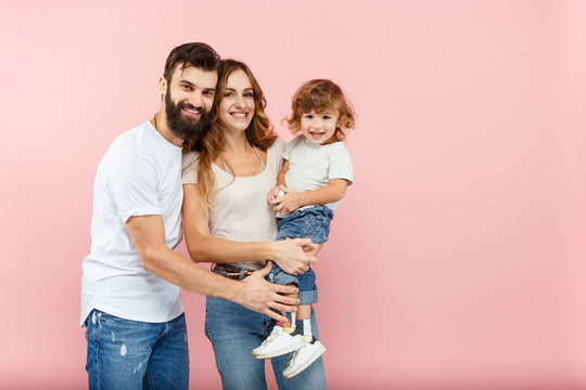 A Happy Family On Pink Studio Background. The Father, Mother And Son Posing Together