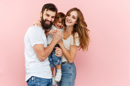 A Happy Family On Pink Studio Background. The Father, Mother And Son Posing Together