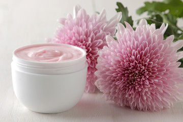 Cream in a white jar close-up and flowers of chrysanthemum on a white wooden table. cosmetics