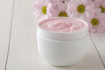 Fototapeta na wymiar Cream in a white jar close-up and flowers of chrysanthemum on a white wooden table. cosmetics