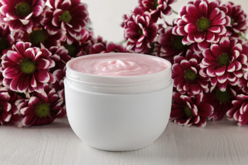 Fototapeta na wymiar Cream in a white jar close-up and flowers of chrysanthemum on a white wooden table. cosmetics