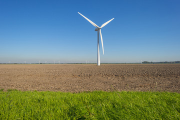 Wind turbine in a plowed field below a blue sky at fall