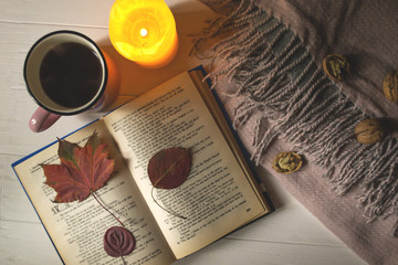 A cup of tea near book and wollen blanket with decoration by fallen leaves. Cozy autumn.