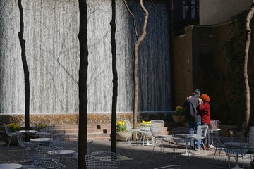 Man and woman watching the waterfall in Paley Pocket Park, midtown Manhattan, New York City, amid yellow tulips and white tables and chairs.