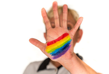 a woman with short blond hair, blurred in a bright background, shows her hand with a painted rainbow